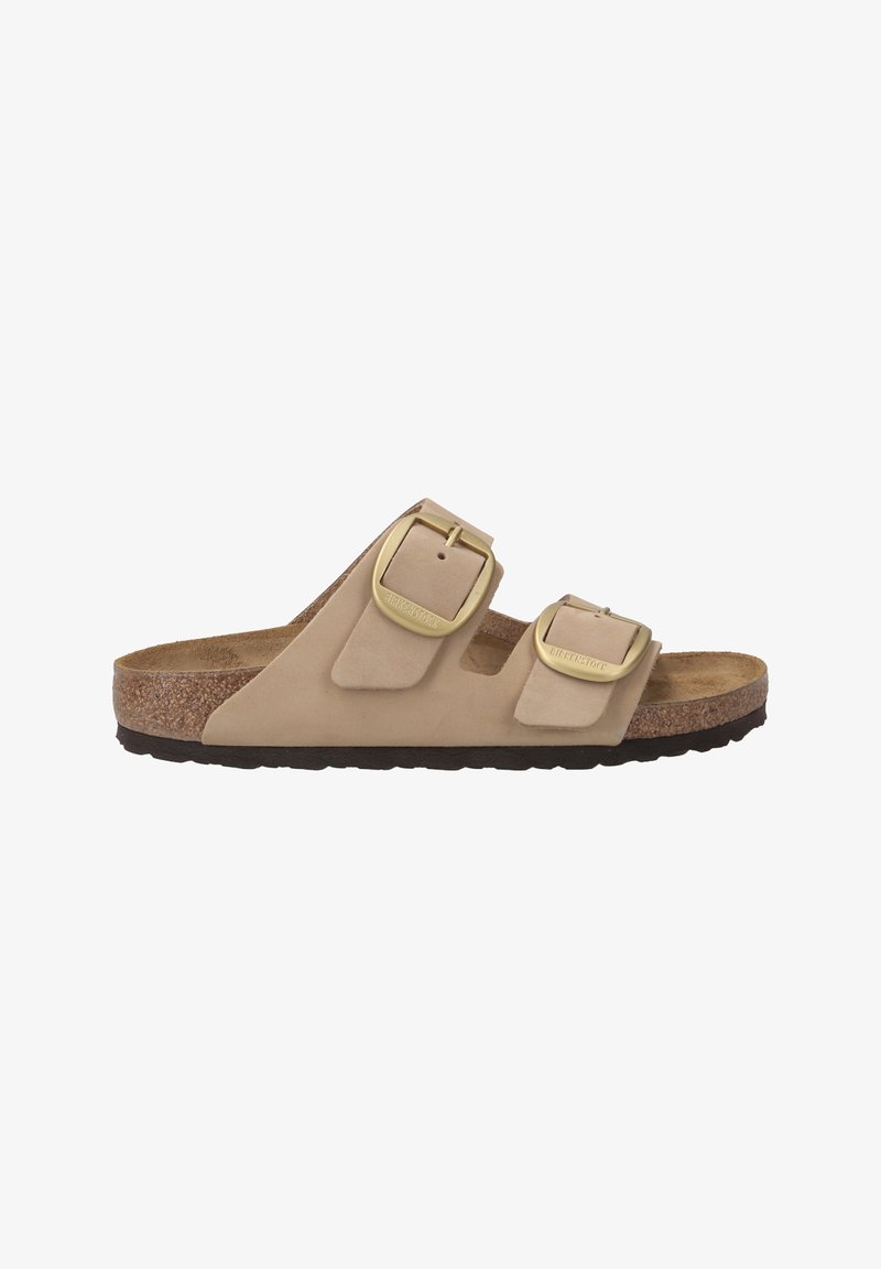 Sandale beige à deux brides avec une tige en suède doux, des boucles en métal doré, un semelle intérieure en liège et une semelle en caoutchouc texturé.