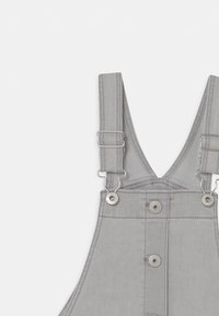 Grå denim overaller med justerbara axelband, metalldetaljer och främre knappstängning. Slät textur med detaljerad sömnad.