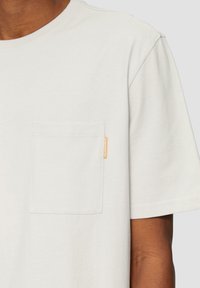 Lichtgrijze t-shirt met korte mouwen, met een borstzakje en een klein oranje label, met een zachte, gladde textuur. Rond de hals.