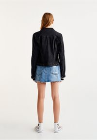 Zwarte spijkerjas met een getailleerd ontwerp, knoopsluiting aan de voorkant en lange mouwen, gecombineerd met een lichtblauwe spijkerrok met rafelige zoom.