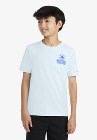 Γαλάζιο βαμβακερό μπλουζάκι με στρογγυλή λαιμόκοψη και κοντά μανίκια. Διαθέτει μπλε γραφικό λογότυπο στο αριστερό στήθος και απλό σχέδιο.