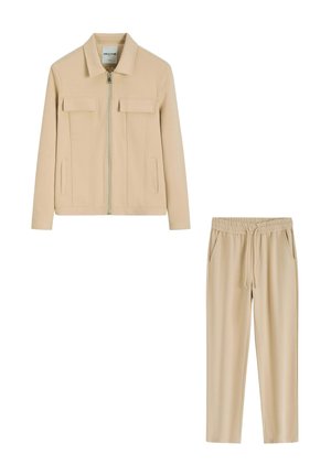 Veste beige avec fermeture éclair à l'avant et poches à rabat, associée à un pantalon beige à taille élastique avec cordon et poches latérales.