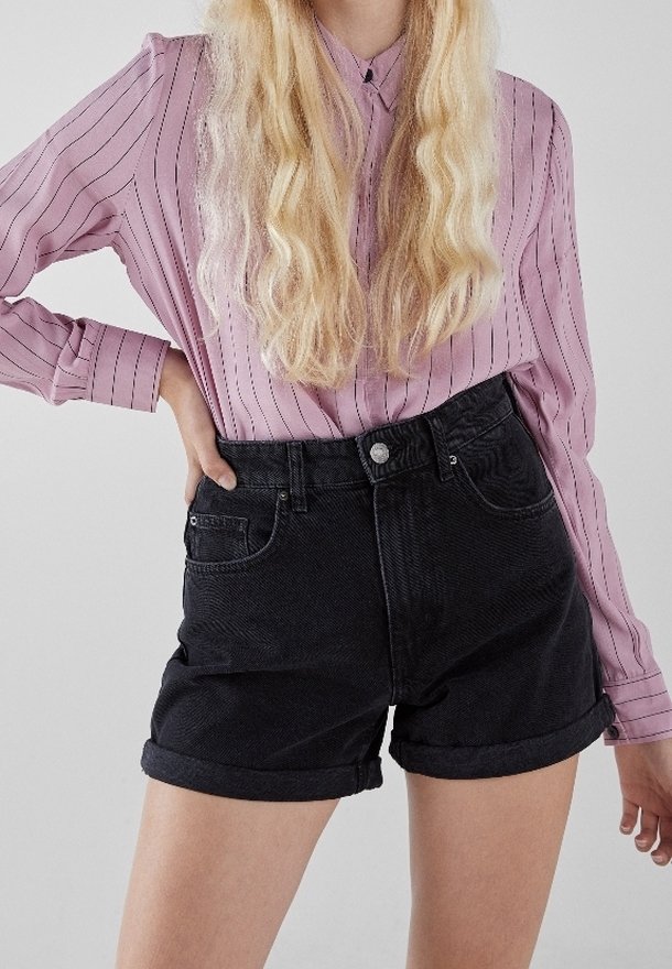 Chemise longue à manches longues de couleur rose clair avec des rayures verticales, assortie à un short en denim noir taille haute, avec des poignets retroussés et des poches avant.