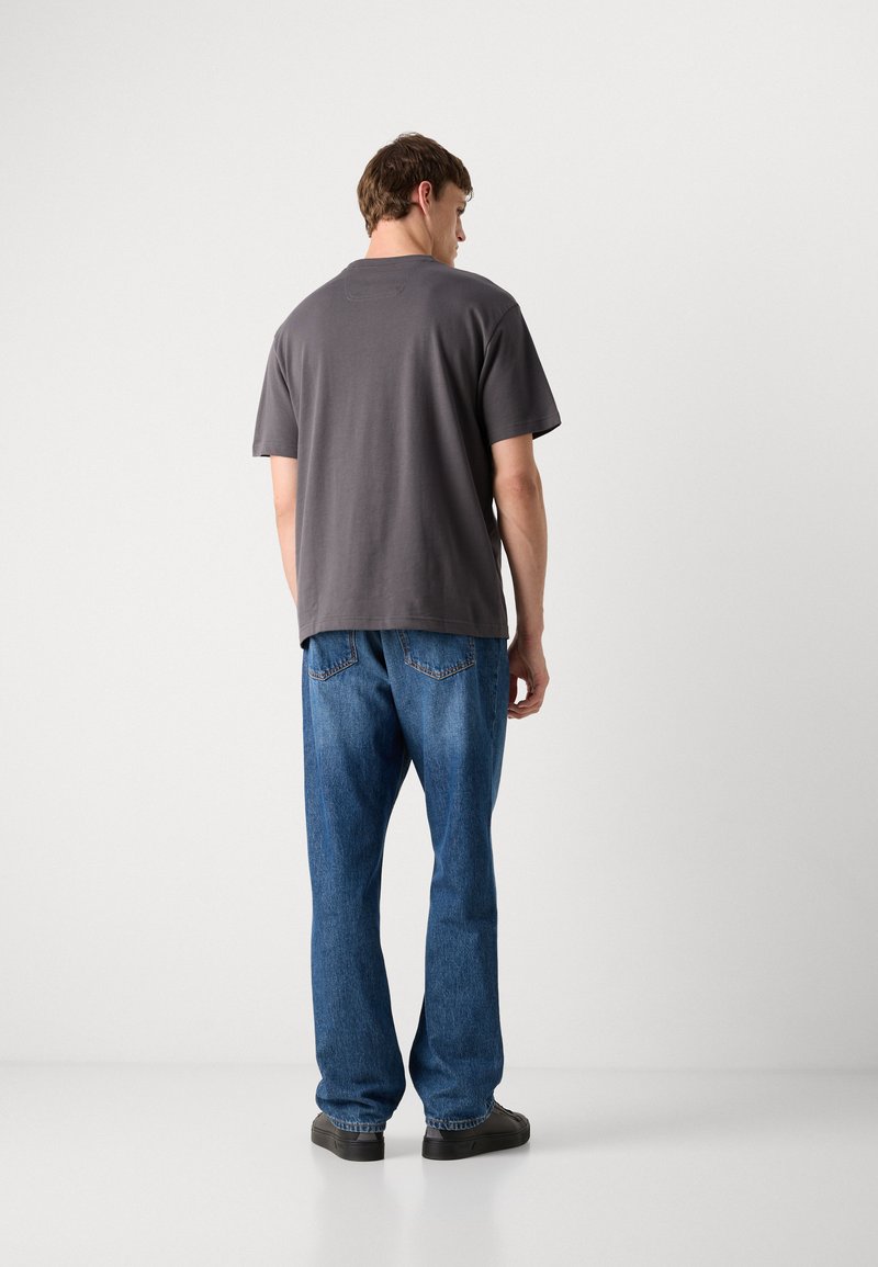 T-shirt en coton gris à manches courtes, associé à un jean en denim bleu. Le t-shirt a une coupe décontractée et le jean est ample.