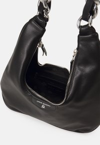 Zwarte leren handtas met een gebogen ontwerp, zilveren rits en kettingband. Heeft een binnenzak en een merklabel. Gladde textuur.