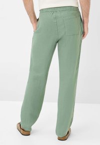 Green linen pants with a relaxed fit, featuring an elastic waistband, back pocket, and light texture. Worn with open-toe sandals.
