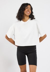 Hvid cropped t-shirt lavet af bomuld med korte ærmer, parret med sorte cykelshorts med høj talje. Enkel design, ingen synlige mønstre.