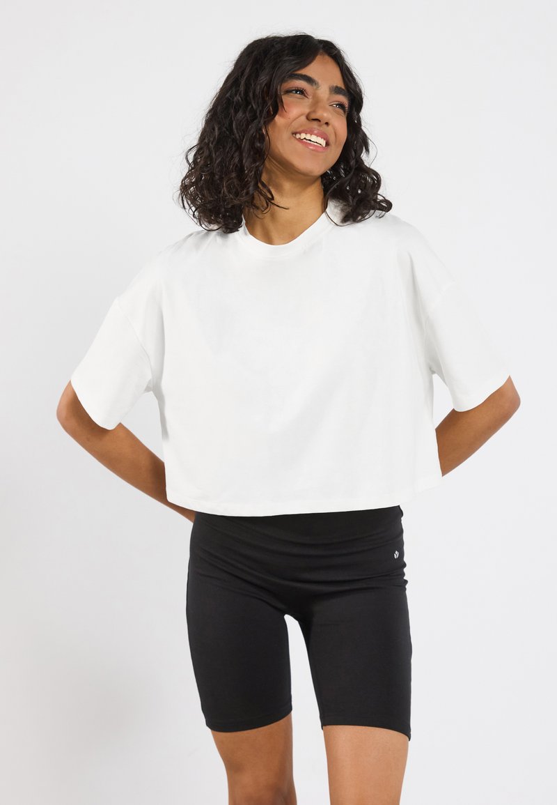 Hvid cropped t-shirt lavet af bomuld med korte ærmer, parret med sorte cykelshorts med høj talje. Enkel design, ingen synlige mønstre.