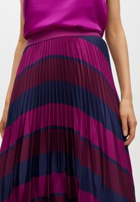 Donna che indossa una gonna a pieghe con strisce curve in tonalità di viola, blu navy e magenta, abbinata a un top magenta a tinta unita.