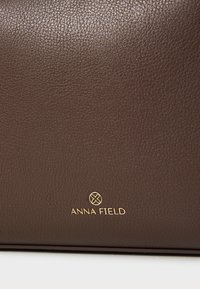 Sac à main en cuir marron avec une finition texturée, arborant un logo doré en relief, conçu pour la durabilité et l'élégance.