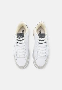 Sneakers bianchi con tomaia in pelle liscia e tessuto, caratterizzati da un accento in suede grigio sulla punta, lacci piatti e un interno color crema.