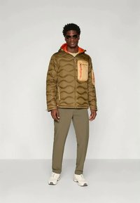 Padded oliwkowa kurtka z pomarańczowymi akcentami, kieszenią na zamek i kapturem, w połączeniu z dopasowanymi oliwkowymi spodniami i białymi sneakery.