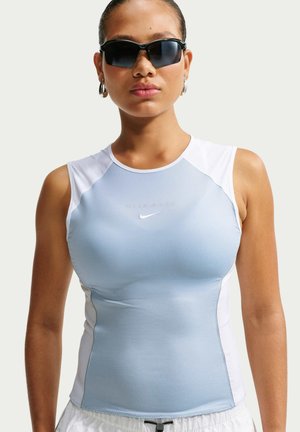 Kvinde iført ærmeløs lyseblå og hvid sportstop med Nike-logo, sorte sporty solbriller og sølv øreringe i hoops, vendt fremad.