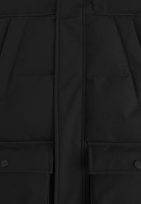 Zwarte gewatteerde vest met een gladde textuur, voorkruiken met drukknoopsluitingen en een centrale ritssluiting. Eenvoudig en functioneel ontwerp.