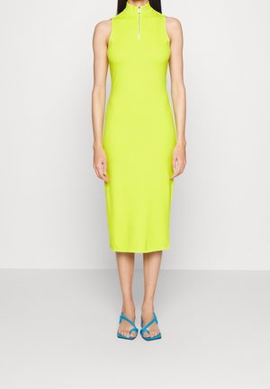 Robe sans manches vert néon avec un col montant et une fermeture éclair à l'avant, design ajusté, atteignant le mollet. Associée à des sandales bleu à lanières.