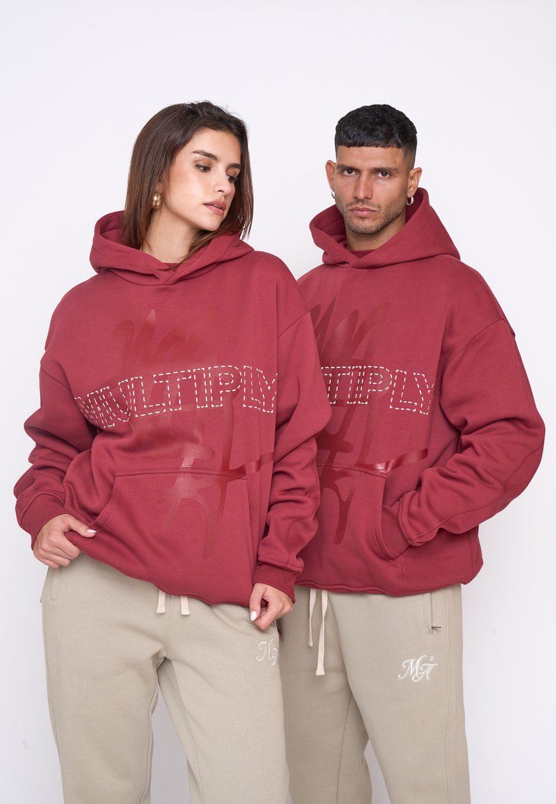 Red hoodies with "MULTIPLY" in white studs and graphics, paired with beige sweatpants featuring embroidered accents. Loose fit and soft texture.