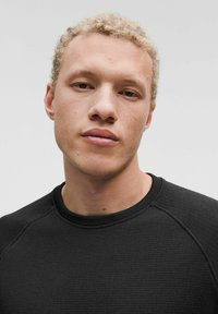 Sudadera negra texturizada con cuello redondo y mangas raglán, que presenta un patrón sutil. Tejido suave con un diseño ajustado.