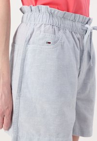 Striped blue shorts with a ruffled waistband, side pockets, and a small brand logo on the front. Made from a lightweight fabric.