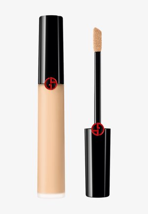Flüssiger Concealer in einem hohen, schwarzen Röhrchen mit glänzender Oberfläche, versehen mit einem roten Logo, und einem Applikator in der Form eines Rehfußes für eine einfache Anwendung.