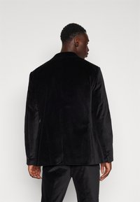 Sacou negru din catifea cu o textură fină, croială ajustată, revere notched și mansete cu nasturi. Design simplu și curat, fără embellishments.