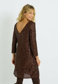 Robe en sequins marron avec des manches longues, décolleté en V à l'arrière et coupe ample, présentant une surface brillante et texturée, et une longueur au genou.