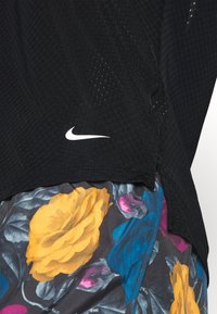 Black mesh athletic shirt with a white Nike logo, layered over floral patterned shorts featuring yellow and blue roses on a dark background.