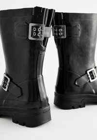 Bottes en caoutchouc noires avec un design haut, boucles en métal argenté, finition texturée et une semelle en caoutchouc robuste avec un motif de crampons.