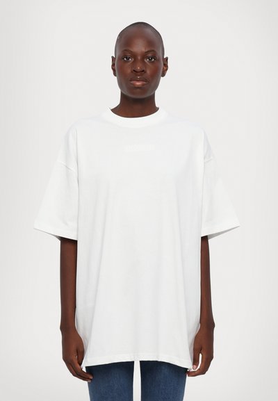T-shirt surdimensionné blanc en coton, avec des manches courtes, un col rond et un logo subtil à l'avant dans un design ton sur ton.