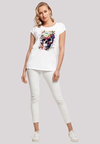 White cotton t-shirt featuring a colorful floral skull graphic. Paired with white skinny jeans and white sneakers. Simple, relaxed fit.