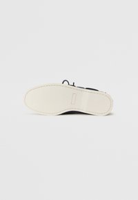Svart skosåle med en glatt, elfenbensfarget gummiyttersåle. Sømdetaljer langs kantene, med et minimalistisk design uten mønstre.