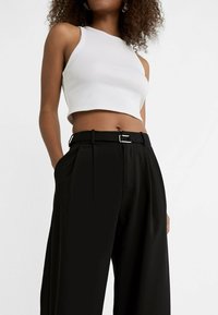 Haut court blanc côtelé avec un col rond, associé à un pantalon noir taille haute à design plissé et une ceinture à boucle argentée.