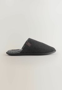 Sorte stofslippers med en tekstureret ribbet overflade, grå blød foring og en sort gummisål. Har et lille logo på siden.