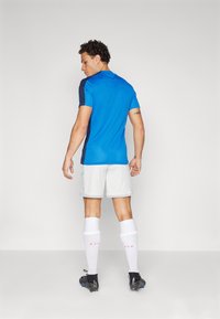 Chemise de sport bleue et bleu marine à manches courtes, shorts blancs et chaussettes blanches. Crampons de football noirs avec des accents. Tissu lisse, coupe athlétique.