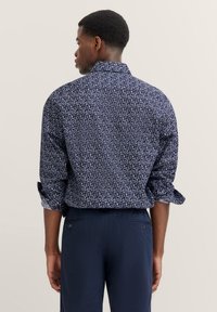 Marineblaues Hemd mit hochgerollten Ärmeln, ausgestattet mit einem geometrischen Muster und einem weichen, strukturierten Stoff. Rückansicht zeigt Kragen und Passformdetails.