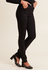 Jeans neri skinny con vita alta, design a cinque tasche e una texture liscia. Abbinati a eleganti scarpe nere con tacco alto.