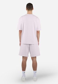 Ensemble en coton rose clair comprenant un t-shirt et un short, au design ample. Texture unie avec des manches courtes et un col rond. Chaussettes de sport blanches et chaussures.