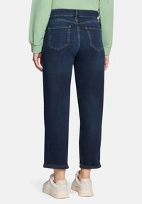 Granatowe dżinsy o luźnym kroju, z pięcioma kieszeniami i podwiniętymi mankietami. Pasek jest elastyczny dla większej wygody.