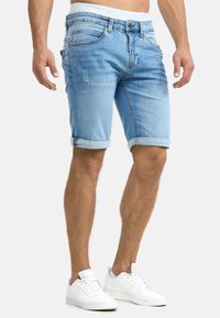 Shorts in denim blu chiaro con risvolti, caratterizzati da un classico design a cinque tasche e un leggero effetto usurato nella parte frontale, abbinati a sneakers bianche.