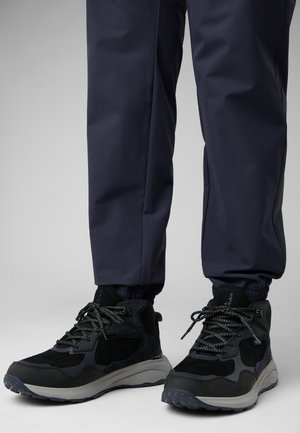 Bottes de randonnée noires avec tige en daim et en mesh, semelle en caoutchouc grise, accents texturés et design à lacets, associées à un pantalon taper bleu marine.