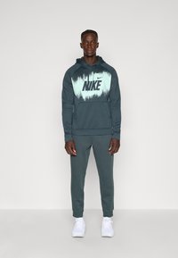 Donker teal Nike hoodie met een gradient turquoise print met het logo. Gecombineerd met bijpassende joggers en witte sportschoenen.