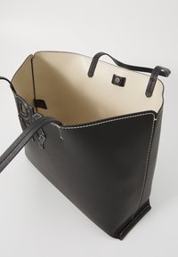 Black leather tote bag with a smooth texture, open top, and contrasting beige lining. Features stitched detailing and two handles.