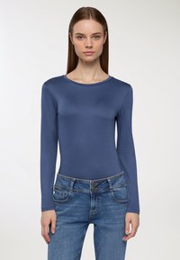 Niebieski body z długim rękawem, uszyte z gładkiego, elastycznego materiału, z okrągłym dekoltem, zestawione z jasnoniebieskimi dżinsami z kieszeniami i podwójnym zapięciem na guziki.