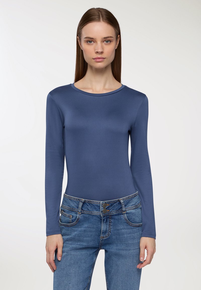 Niebieski body z długim rękawem, uszyte z gładkiego, elastycznego materiału, z okrągłym dekoltem, zestawione z jasnoniebieskimi dżinsami z kieszeniami i podwójnym zapięciem na guziki.