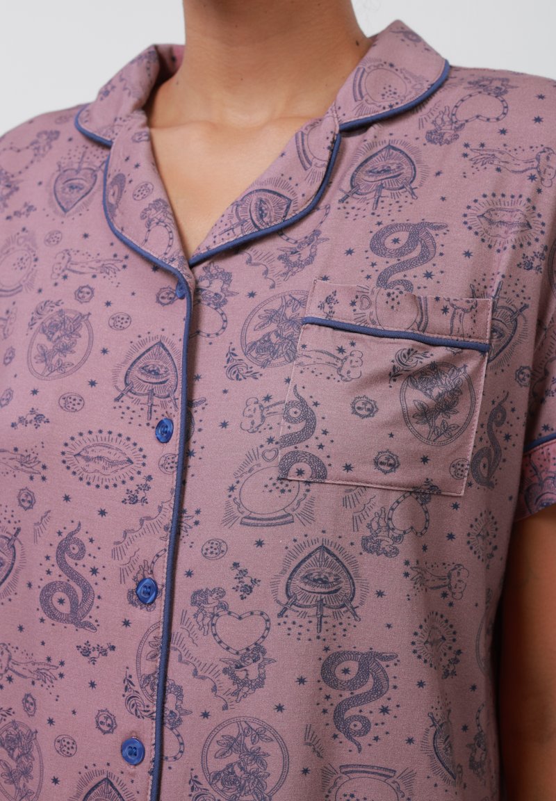 Maglietta da pigiama a maniche corte in lavanda con tasca, bordi blu navy e vari motivi blu scuro, tra cui design celestiali e floreali.