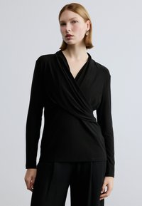 Zwarte blouse met lange mouwen en een overslagontwerp, met een zachte textuur en een V-hals. De stof lijkt glad en aansluitend te zijn.