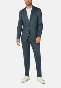 Dunkelblaues Anzug mit strukturiertem Finish, einreihiger Blazer, mit Reverskragen, passende Hose, kombiniert mit weißen Sneakers.