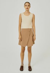 Krämsribbat stickat ärmlöst linne som kombineras med en beige omslagskjol med två knappar och sidficka. Modellen har på sig bruna skor och strumpor.