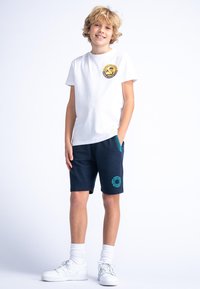 Biała bawełniana koszulka z okrągłym żółtym logo na klatce piersiowej, zestawiona z granatowymi szortami z turkusowymi akcentami i bocznymi kieszeniami.