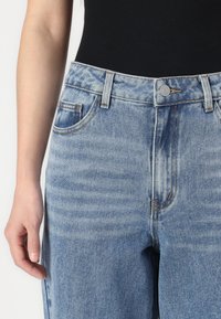Vaqueros de denim de color azul claro con un diseño de pierna recta, que cuentan con bolsillos delanteros, un cierre de botón y un detalle de costura en contraste.