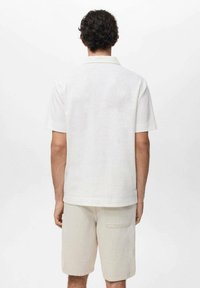 Kortærmet, hvid skjorte med en subtil tekstur og en foldet krave, parret med lyse beige shorts med en baglomme.